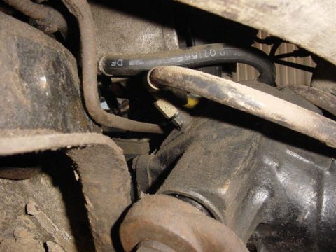 1992 Ford Bronco - Grimy underside close-up around a front axle, showing the cast differential housing, a rubber vent or brake hose with a printed part number…