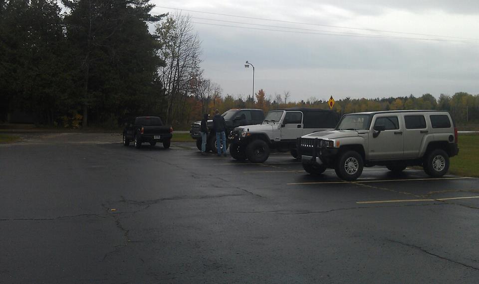 Silver Hummer H3 and white Jeep parked in a lot with a black pickup truck