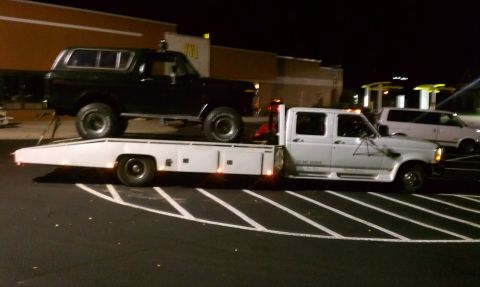 1979 Ford Bronco - A black 1978 Ford Bronco is loaded onto a white flatbed tow truck, with a white van visible in the background.