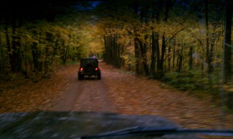 1979 Ford Bronco - A black SUV drives down a dirt road lined with trees in autumn.