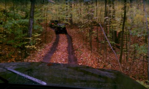 1979 Ford Bronco - An off-road vehicle navigates a muddy, leaf-strewn path through a forest during autumn.
