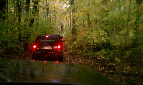 1979 Ford Bronco - A black SUV with a Monster Energy sticker drives down a wooded dirt road during autumn.