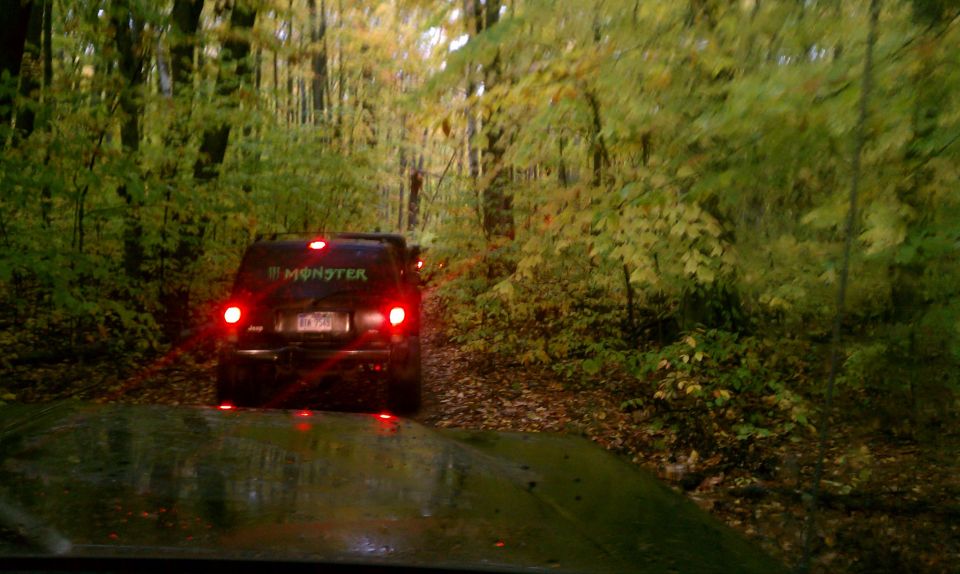 Black SUV with Monster Energy sticker on rear window, driving on a dirt road in a forest