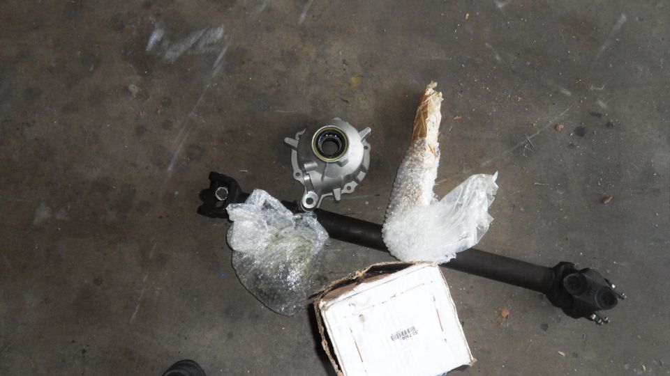 Driveshaft and differential parts on concrete floor. Includes a metal housing and a long shaft