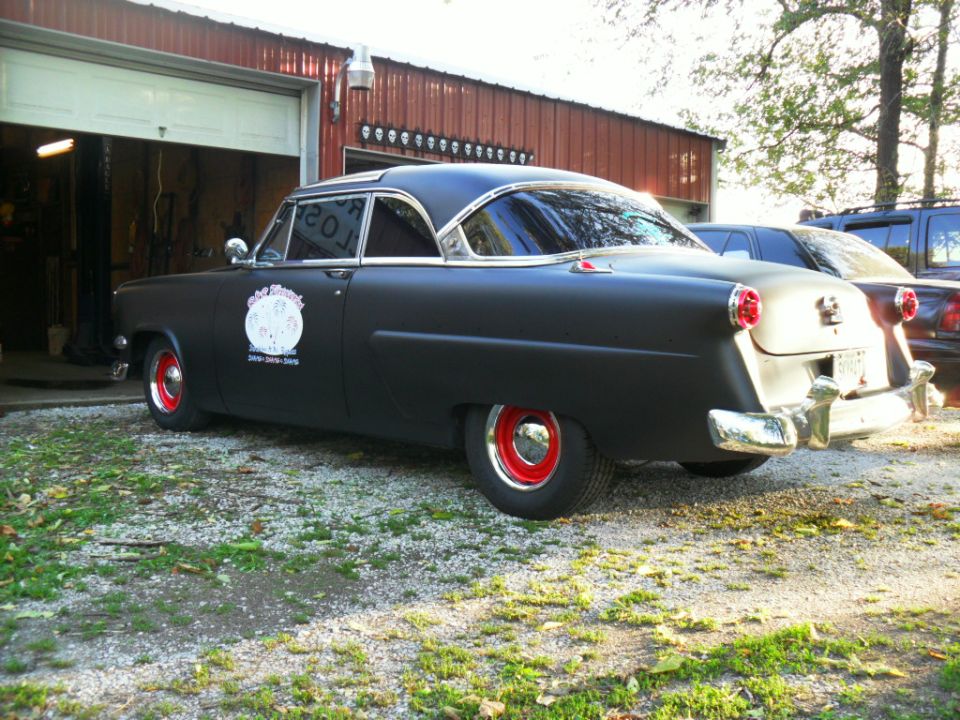 black coupe with red wheels parked outside a garage, another vehicle behind it