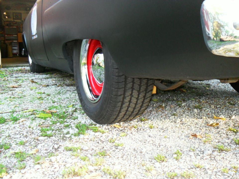 Rear wheel with red rim and chrome hubcap on matte black car