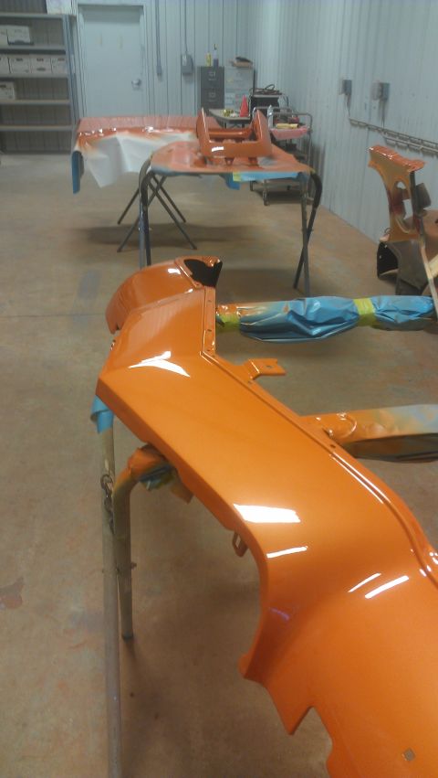 1973 Chevrolet Camaro - A freshly painted orange car bumper is drying in a workshop, with other parts visible in the background.