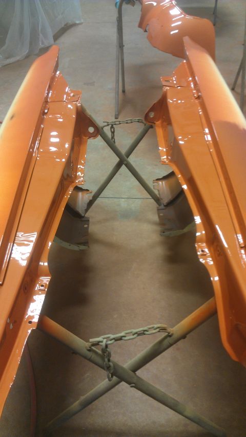 1973 Chevrolet Camaro - Car fenders are suspended on stands, undergoing a fresh coat of orange paint in a workshop.
