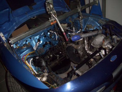 1995 Ford Probe - Engine bay of a blue car is shown with the engine removed and an engine hoist positioned above.