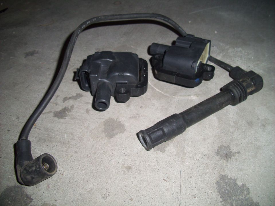 Two black ignition coils and one spark plug wire on a concrete surface