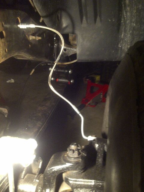 1995 Ford Bronco - Close-up view of the undercarriage, focusing on brake lines and suspension components with a jack stand in the background.