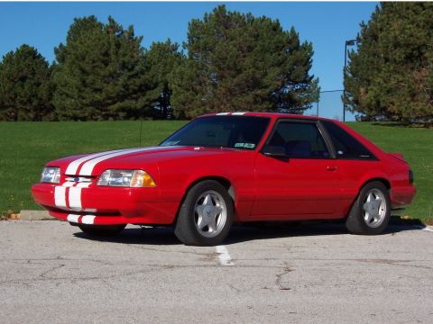 1990 Ford Mustang - This red 1990 Ford Mustang coupe displays white racing stripes and is viewed from a three-quarter front angle.