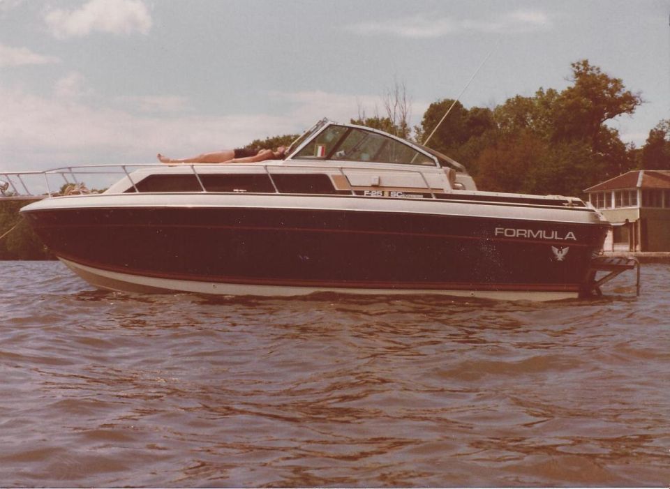 Dark blue and white Formula boat with a person sunbathing on deck, side view