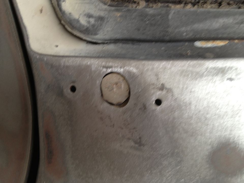 Close-up of a vehicle's metal body panel with a bolt and two small holes, possibly undergoing repair