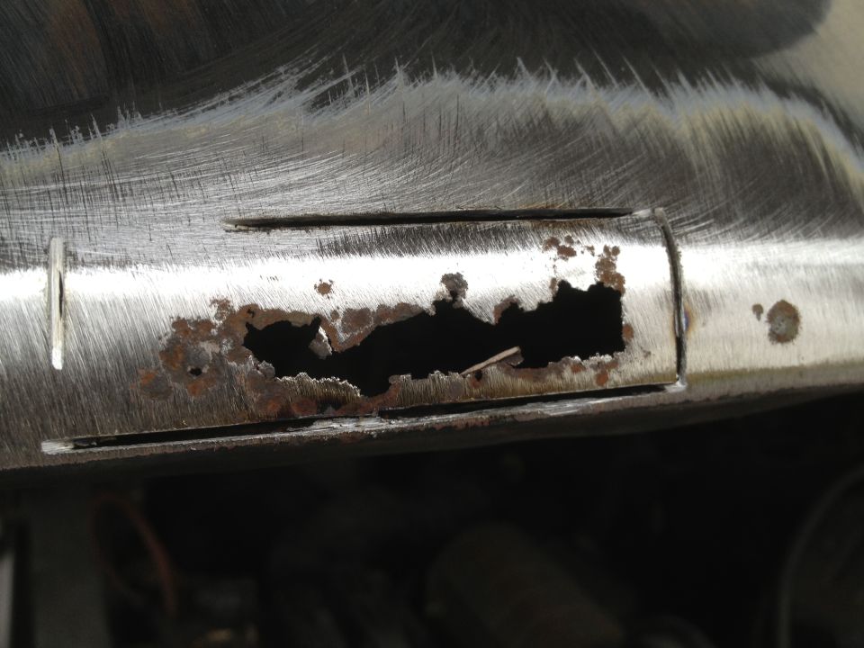Close-up of a corroded metal panel with a large hole, showing rust and scratches