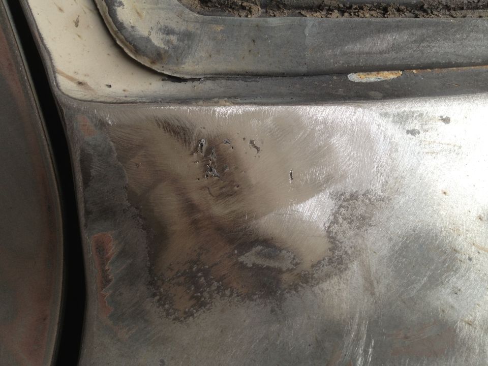 Close-up of a sanded and prepped metal body panel, likely for repair, showing some rust spots and primer