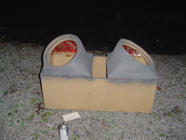 Homemade subwoofer enclosure box with two angled ports, primer-gray finish, on gravel at night
