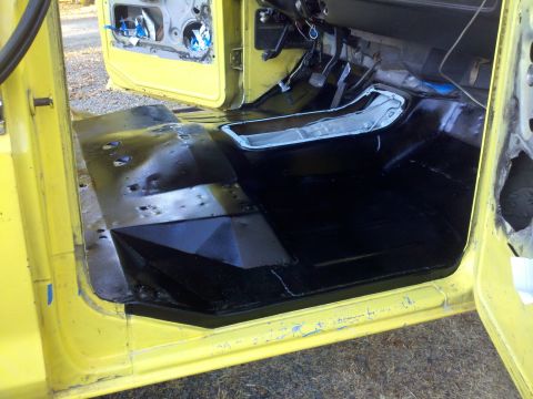 1978 Ford Bronco - Interior floor of a yellow vehicle, showing black coating and exposed door mechanisms.
