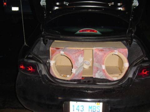 1999 Ford Taurus - The rear of a black car is shown with the trunk open, revealing a partially constructed speaker box.