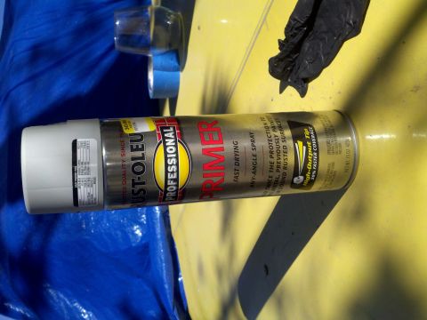 1978 Ford Bronco - A can of primer rests on a yellow surface, with a blue tarp and black gloves nearby.