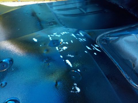 1978 Ford Bronco - Close-up view of a vehicle's interior floor pan, showing a dark blue painted surface with white paint splatters and circular indentations.