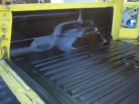 1978 Ford Bronco - The interior of a yellow truck bed shows a freshly applied black spray-in liner.