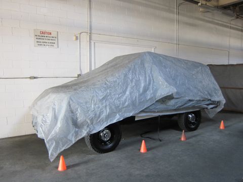 1987 Dodge 1500 - A vehicle is covered by a tarp in an indoor setting with caution signage on the wall.