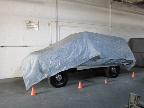 1987 Dodge 1500 - A vehicle is covered by a large tarp, with orange cones placed around its perimeter inside a building.