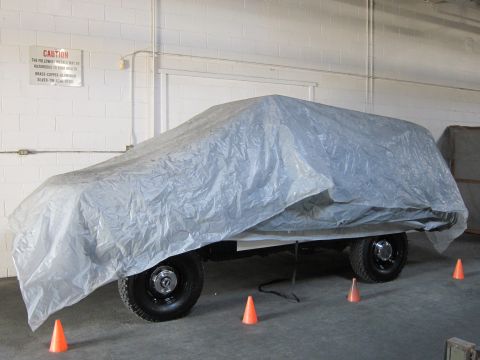 1987 Dodge 1500 - A vehicle covered by a tarp sits in a warehouse, with caution signs on the wall.
