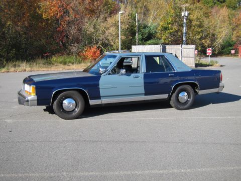 1991 Ford LTD Crown Victoria - A two-tone blue 1991 Ford Crown Victoria is parked in an asphalt lot with autumn trees in the background.