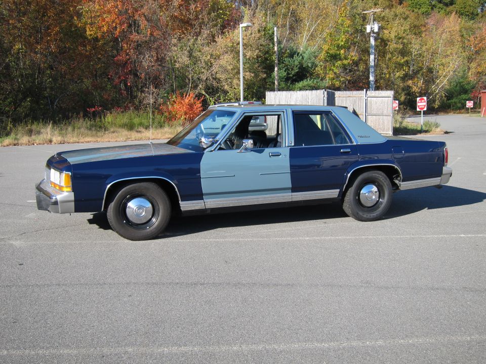 Side view of a 1991 Ford Crown Victoria with two-tone blue paint. It has steel wheels with chrome hubcaps