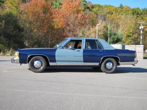 1991 Ford LTD Crown Victoria - A two-tone blue sedan is parked outdoors with trees in the background.