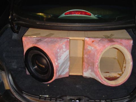 1999 Ford Taurus - A custom fiberglass and MDF dual subwoofer enclosure test-fitted in an open car trunk, with pink body filler skimmed over the glassed baffl…