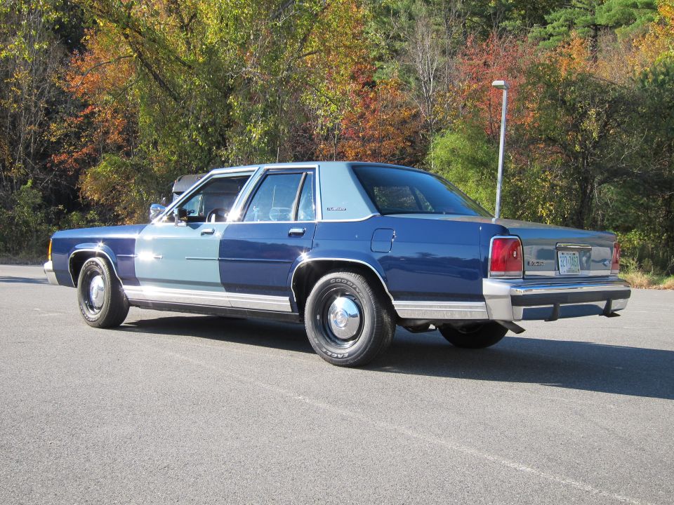 Rear 3/4 view of a two-tone blue Ford Crown Victoria. The rear license plate is visible