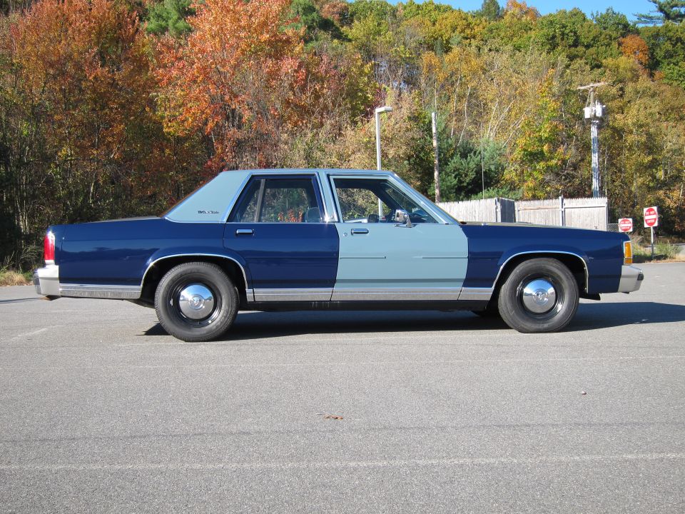 Two-tone blue sedan, light blue front half, dark blue rear half, chrome hubcaps, parked on asphalt
