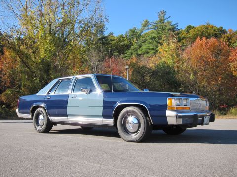 1991 Ford LTD Crown Victoria - A two-tone Ford Crown Victoria is parked on an asphalt surface with autumn foliage behind it.