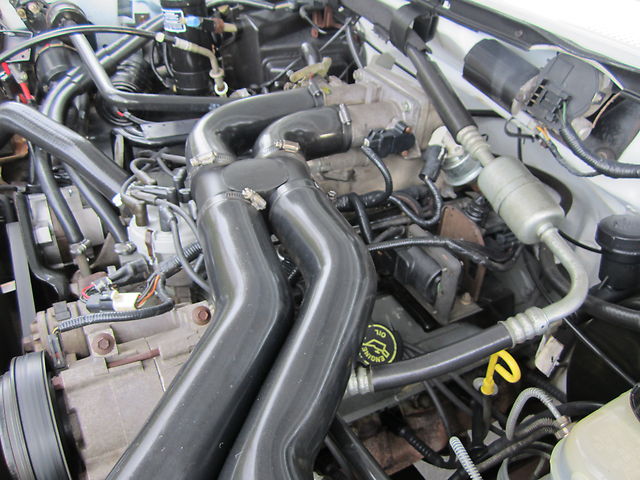 Engine bay with large black intake tubes and an oil cap that says 'Ford'