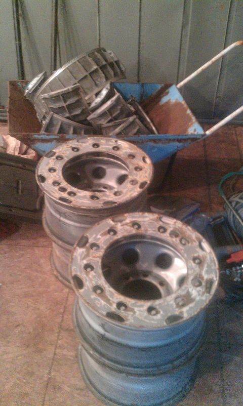 1995 Ford Bronco - Several truck wheels are stacked, with various metal parts piled in a wheelbarrow.
