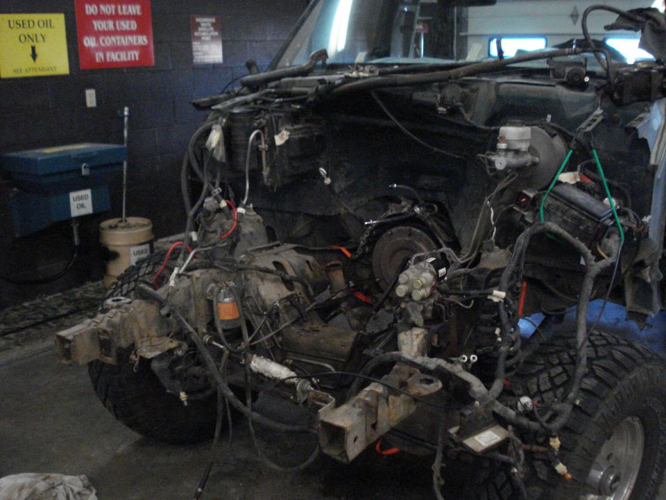 Disassembled vehicle chassis with exposed engine components and wiring, viewed from the front