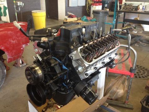 1994 Ford Bronco - Engine assembly on a stand in a workshop, with a red fender from another vehicle visible to the left.