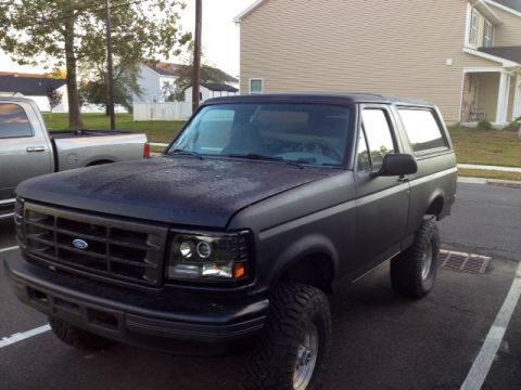 1994 Ford Bronco - A matte black Ford Bronco is parked in a lot next to a silver pickup truck.