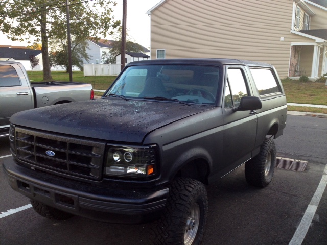 Dark matte Ford Bronco with lifted suspension and aftermarket headlights parked next to a silver pickup truck