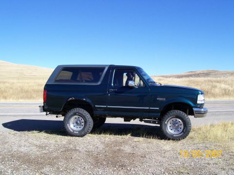 Dark green Ford Bronco parked on the side of a road with dry grass and hills in the background