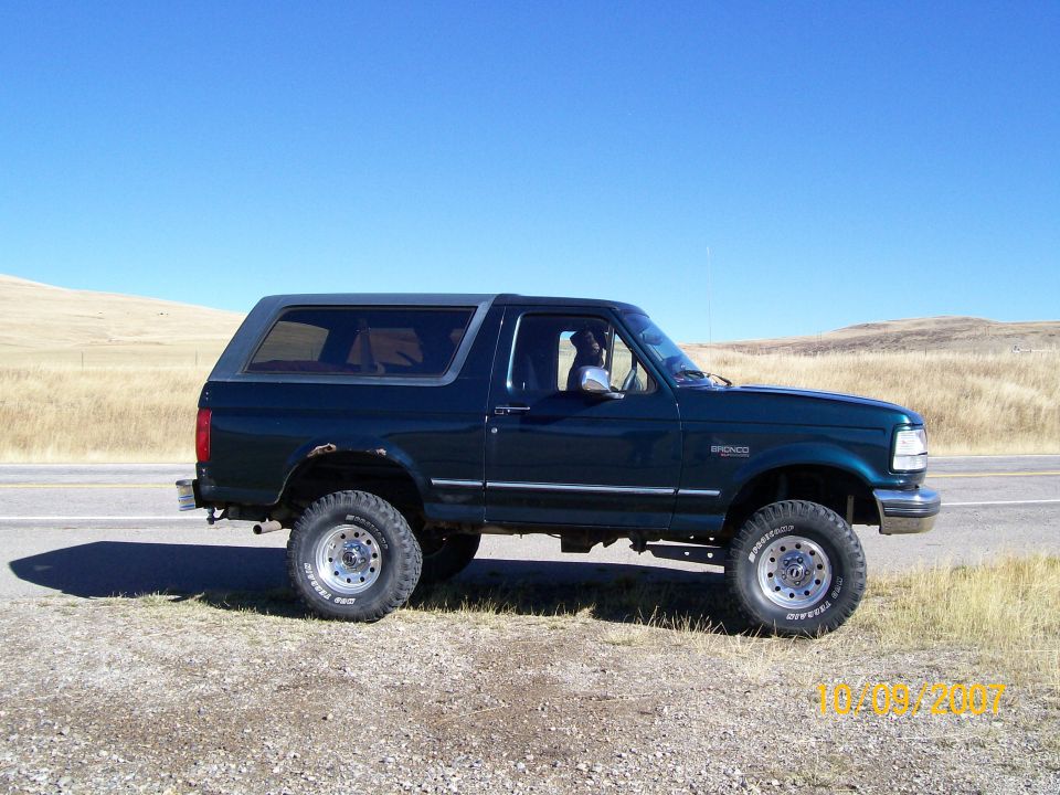 Dark green Ford Bronco parked on the side of a road with dry grass and hills in the background