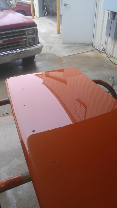 1973 Chevrolet Camaro - An orange car part is mounted on a rack, with a reflection of a building visible on its surface.