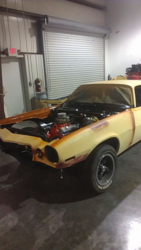 1973 Chevrolet Camaro - A classic Chevrolet Camaro is shown in a garage with its hood open, revealing the engine during what appears to be a restoration process.