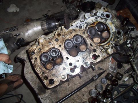 1995 Ford Probe - A close-up view of a dirty engine cylinder head with valves, with a drill tool positioned to work on it.