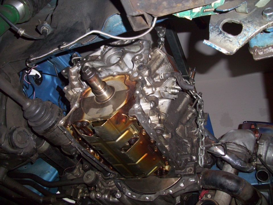 Engine assembly suspended by chains, showing oil pan and drive axle components