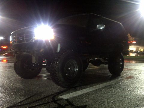 1995 Ford Bronco - This lifted 1995 Ford Bronco is captured at night, its bright headlights illuminating the wet parking lot.