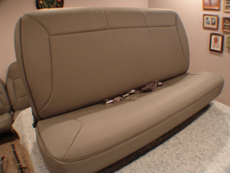 Tan leather bench seat with visible seatbelts, angled from the side